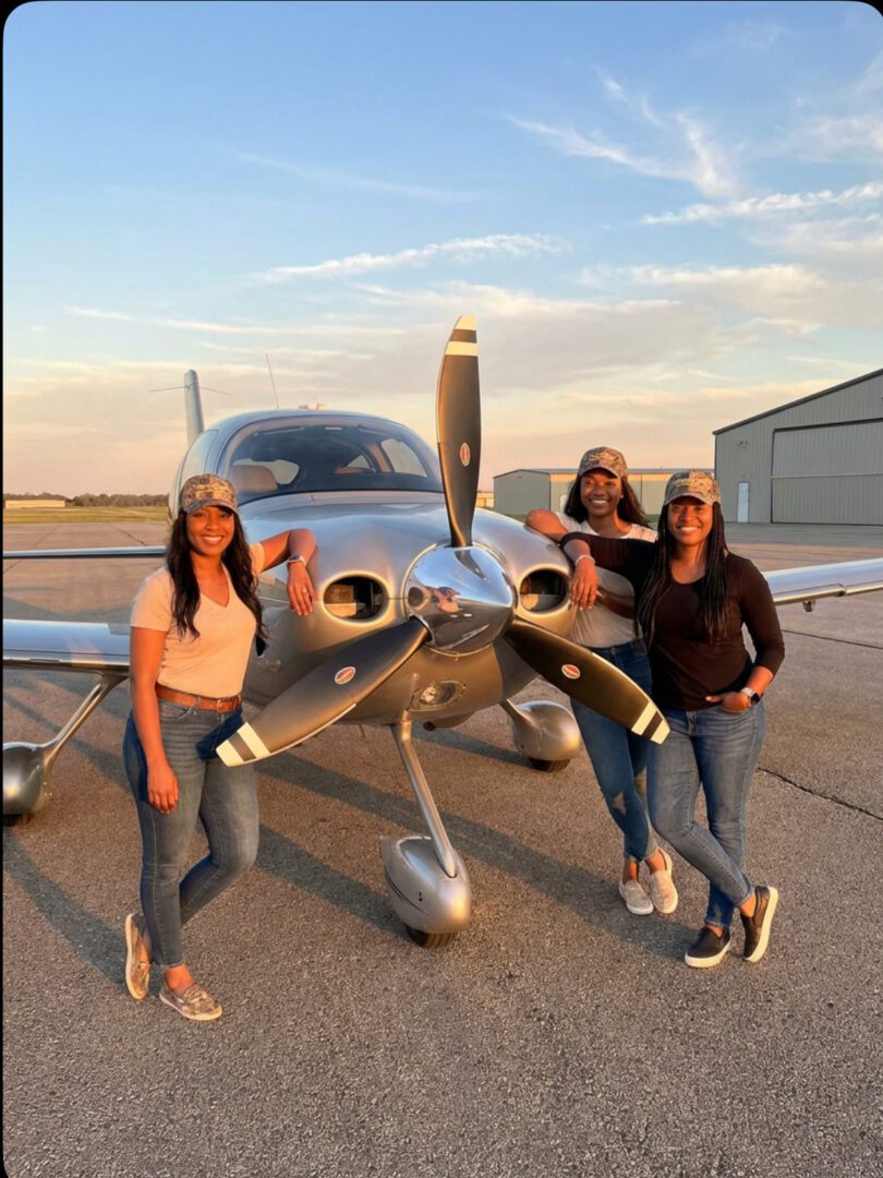 Three people posing with small airplane.